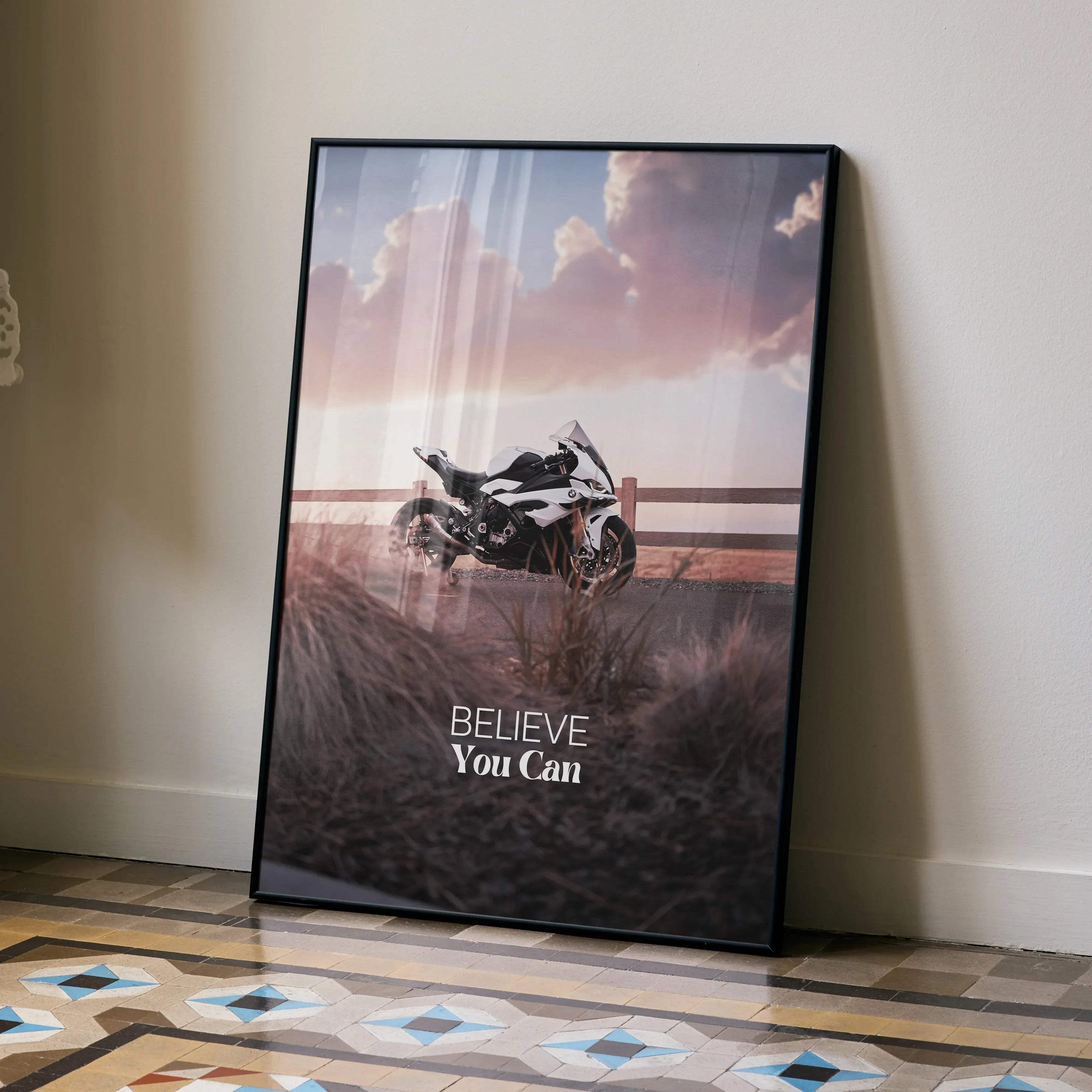 Black-framed motivational poster of a white and black bmw inspired s1000rr motorcycle under a pink sky with believe you can text