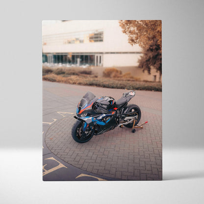Canvas art of a BMW M1000RR motorcycle parked on a brick driveway with building and trees in background wall art.