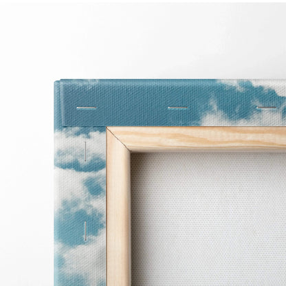 Corner detail of stretched canvas wall art with blue sky and white clouds, natural wood frame.