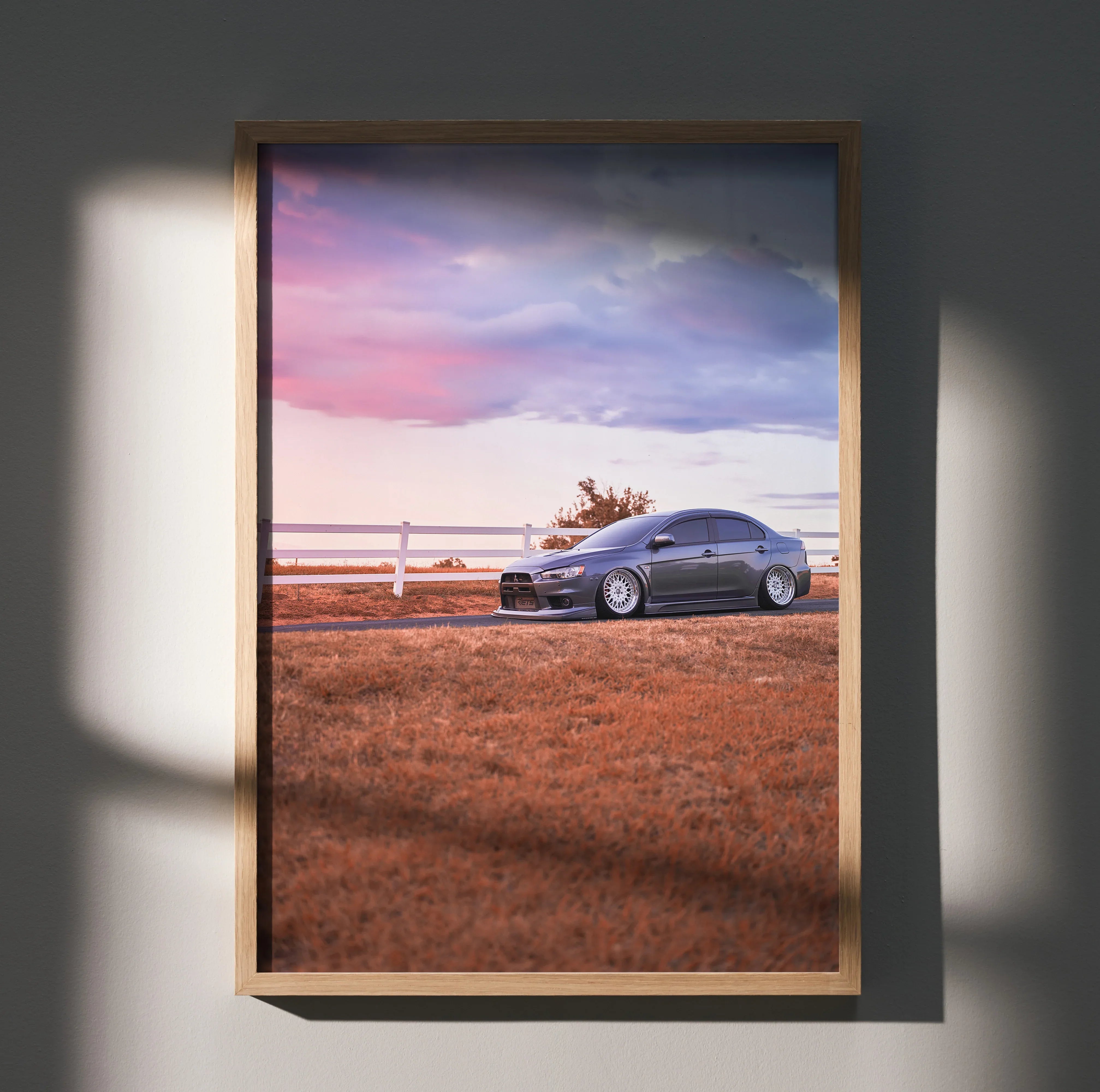 Mitsubishi Evo 10 parked on grassy field at sunset poster wall art in wooden frame.