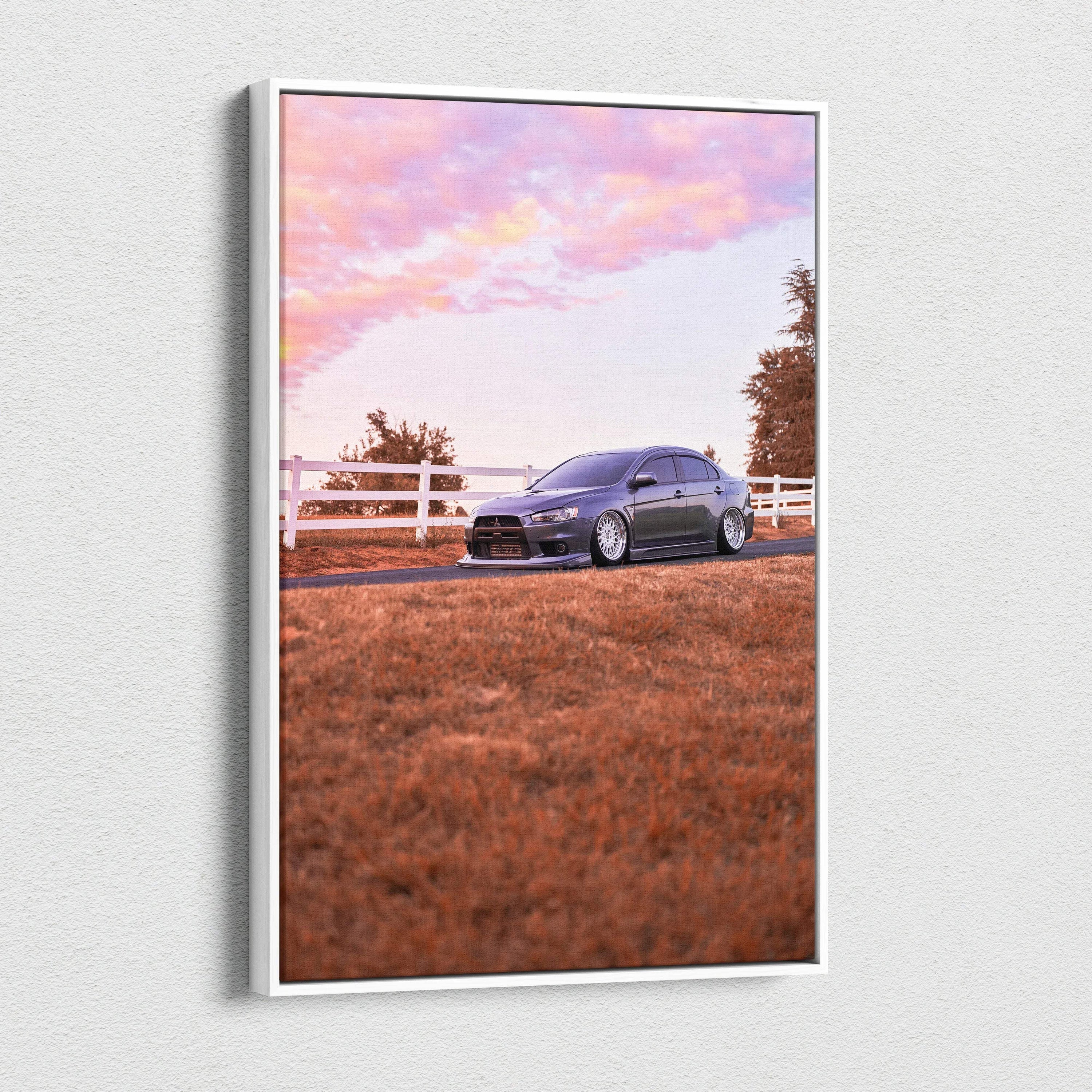 Vertical canvas wall art of a dark Mitsubishi Evo 10 parked on grass with a white fence and pink sunset sky.
