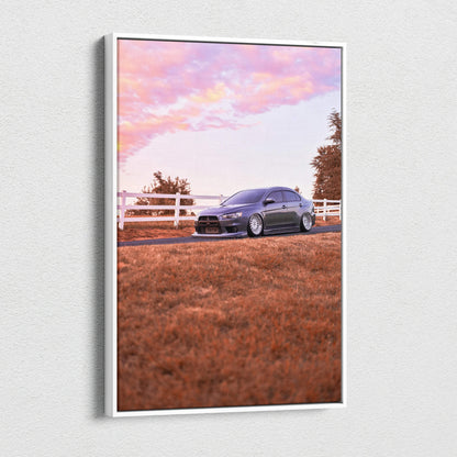 Vertical canvas wall art of a dark Mitsubishi Evo 10 parked on grass with a white fence and pink sunset sky.
