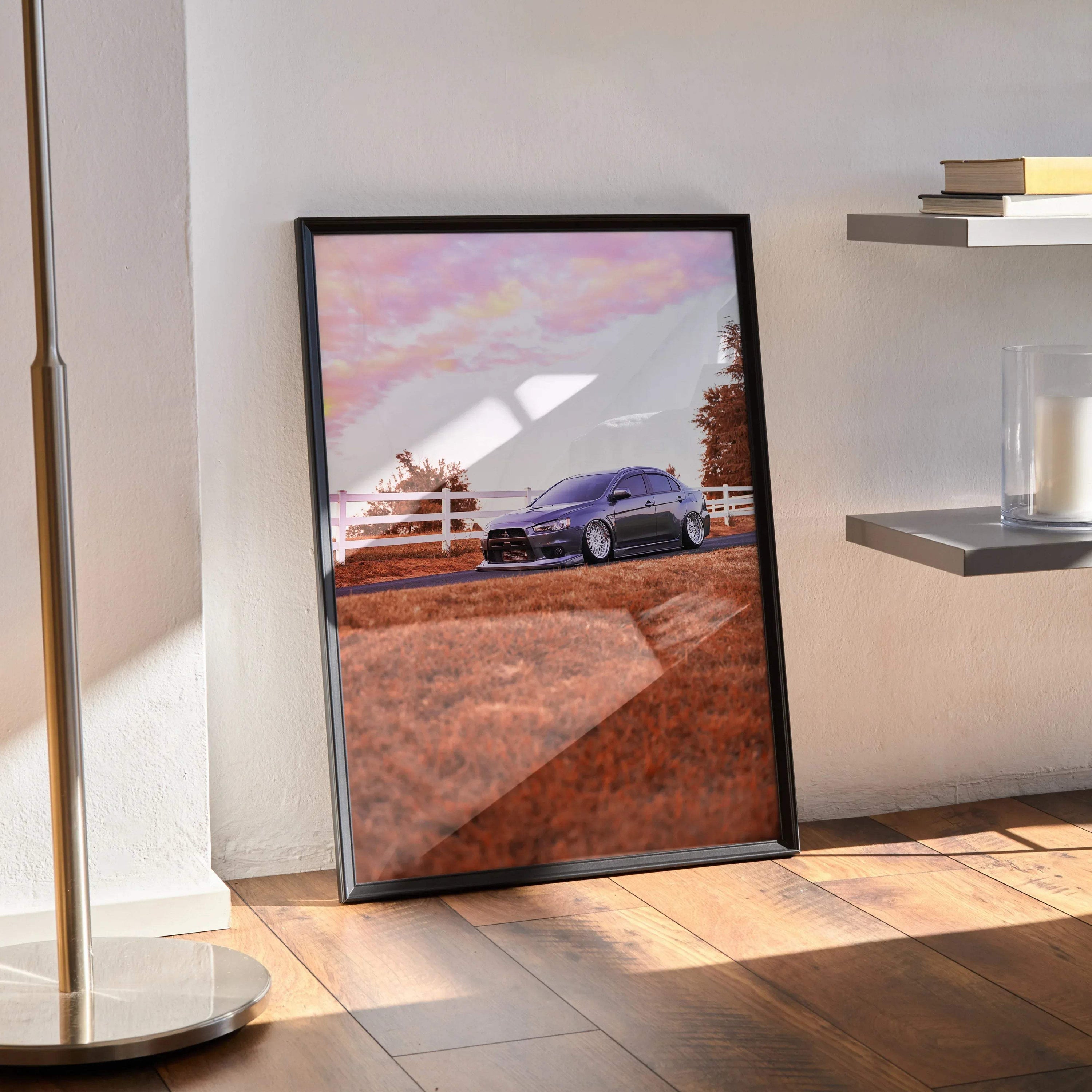 Framed Mitsubishi Evo 10 poster leaning on floor with scenic road and pink sky wall art.