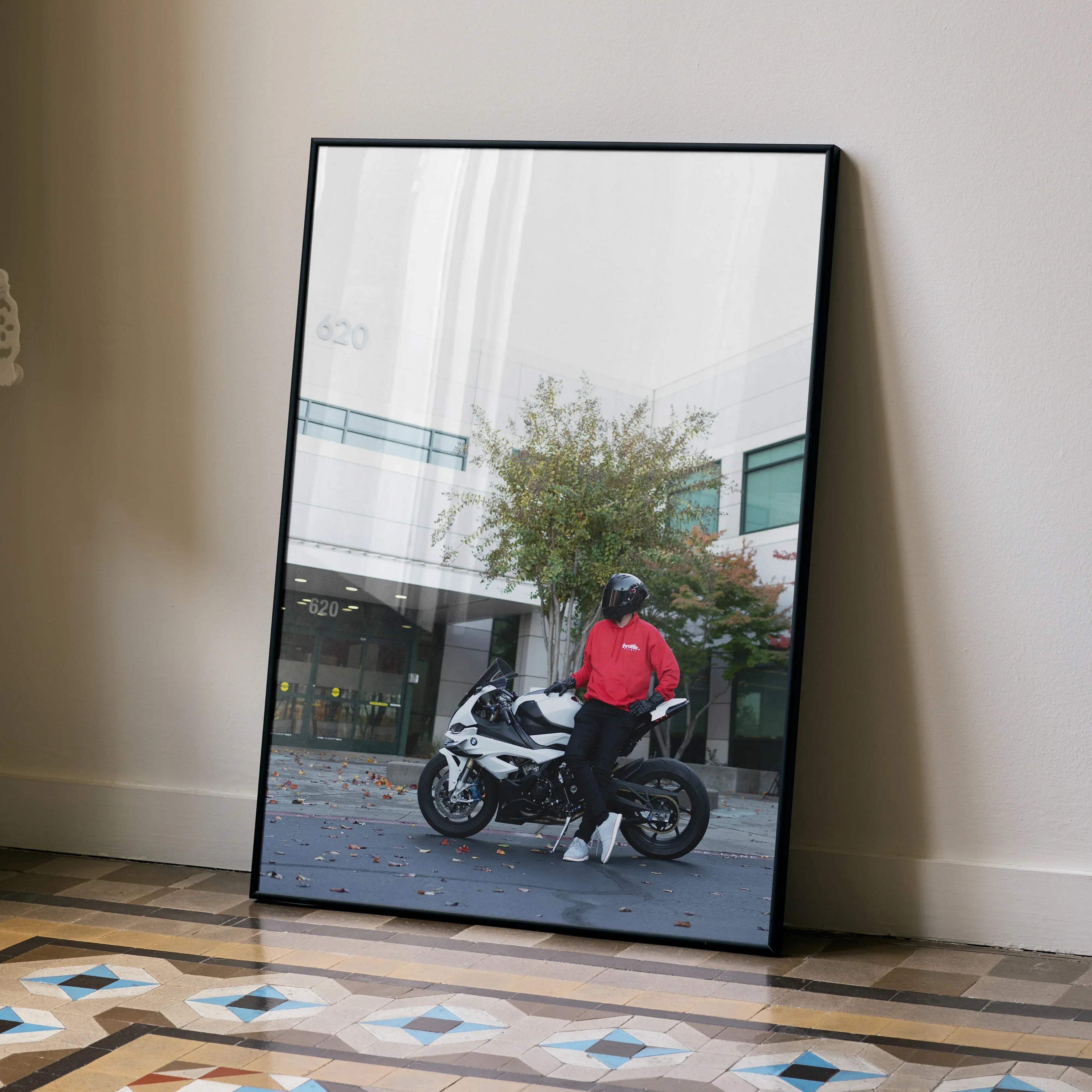 Black-framed biker poster showing male in red hoodie with shark aeron gp helmet on white bmw s1000rr motorcycle