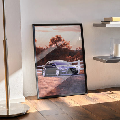 Mitsubishi Evo 10 poster wall art featuring a sleek silver car parked by a white fence at sunset with warm tones.