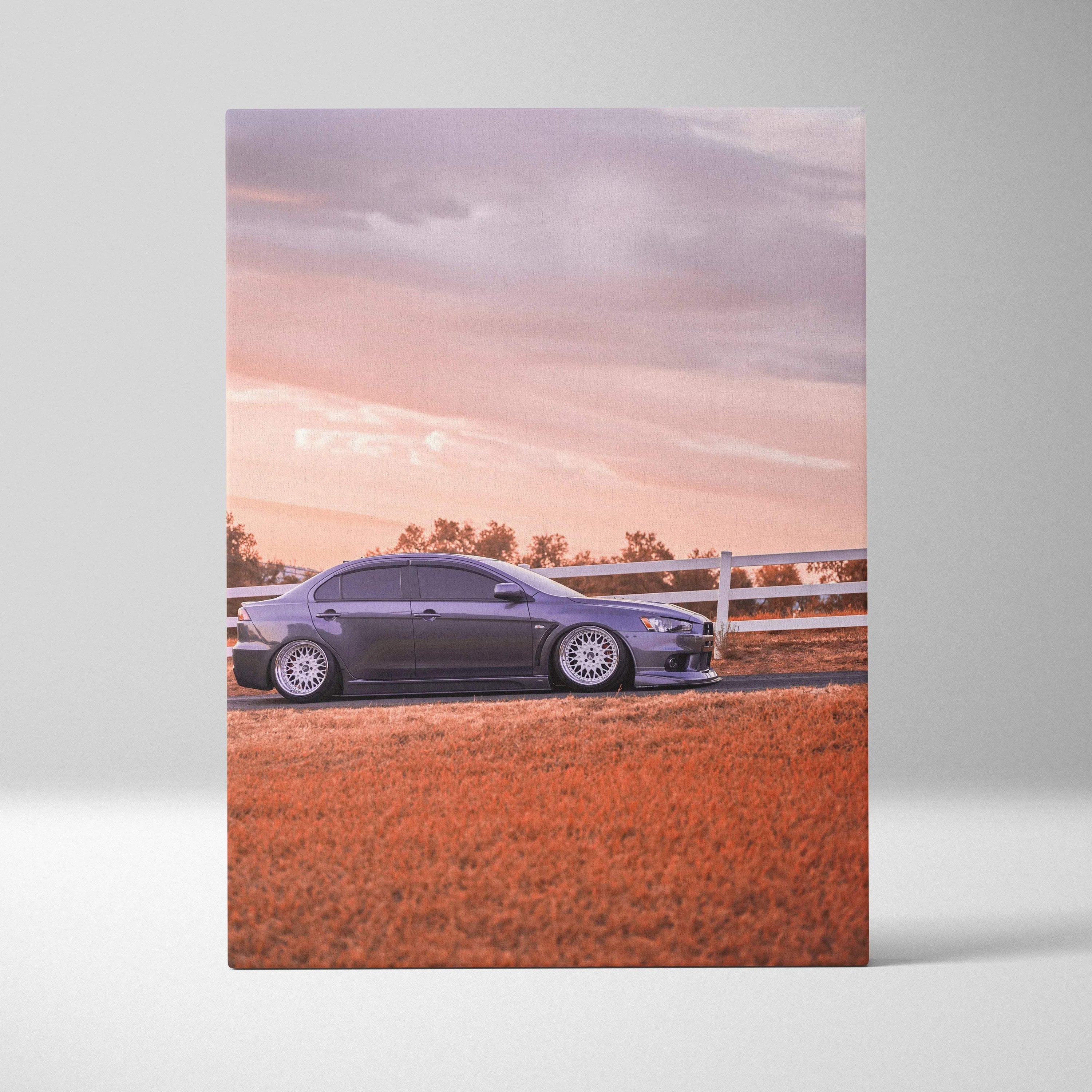 Vertical canvas art of a sleek black Mitsubishi Evo 10 parked on a reddish field at sunset.
