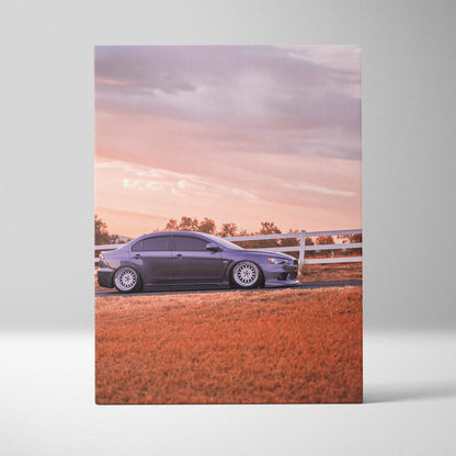 Vertical canvas art of a sleek black Mitsubishi Evo 10 parked on a reddish field at sunset.
