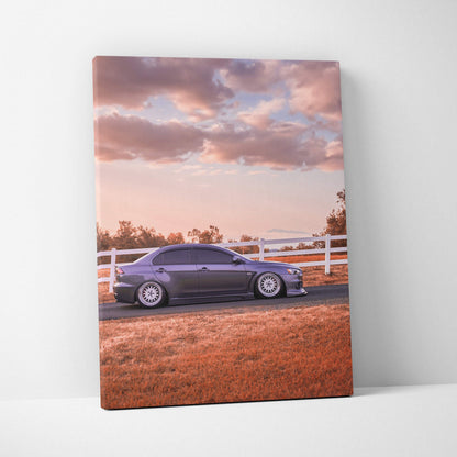Vertical canvas art of a blue Mitsubishi Evo 10 parked by a white fence under a pink and purple sunset sky.