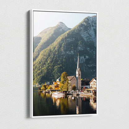 Framed canvas wall art showing a serene lakeside village with a church steeple, surrounded by forested mountains and.