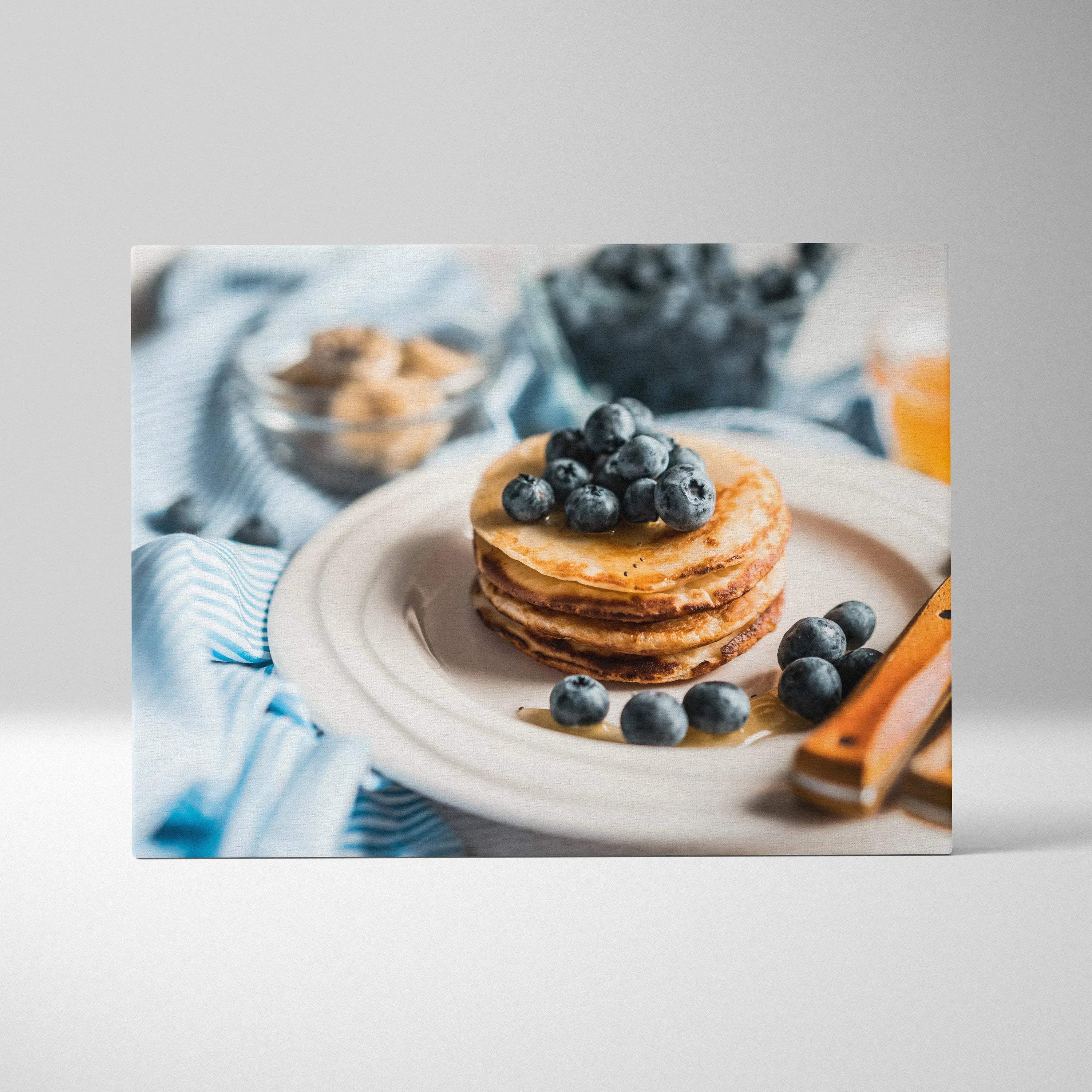 Canvas wall art featuring a stack of golden pancakes topped with fresh blueberries on a white plate with cinnamon sticks and