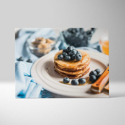 Canvas wall art featuring a stack of golden pancakes topped with fresh blueberries on a white plate with cinnamon sticks and