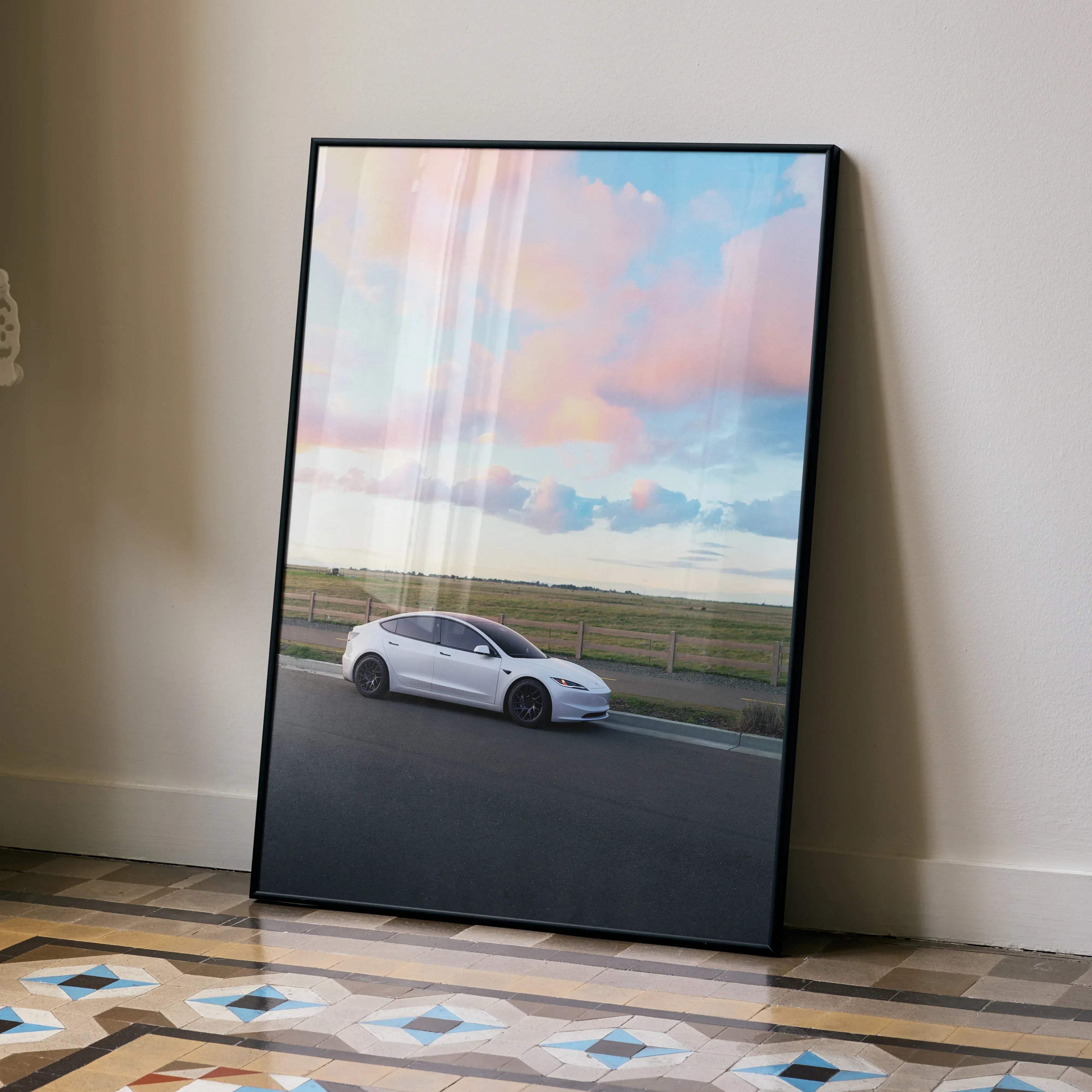 Black-framed poster of white tesla model 3 driving under pastel pink and blue sky titled tesla model 3 highland car poster