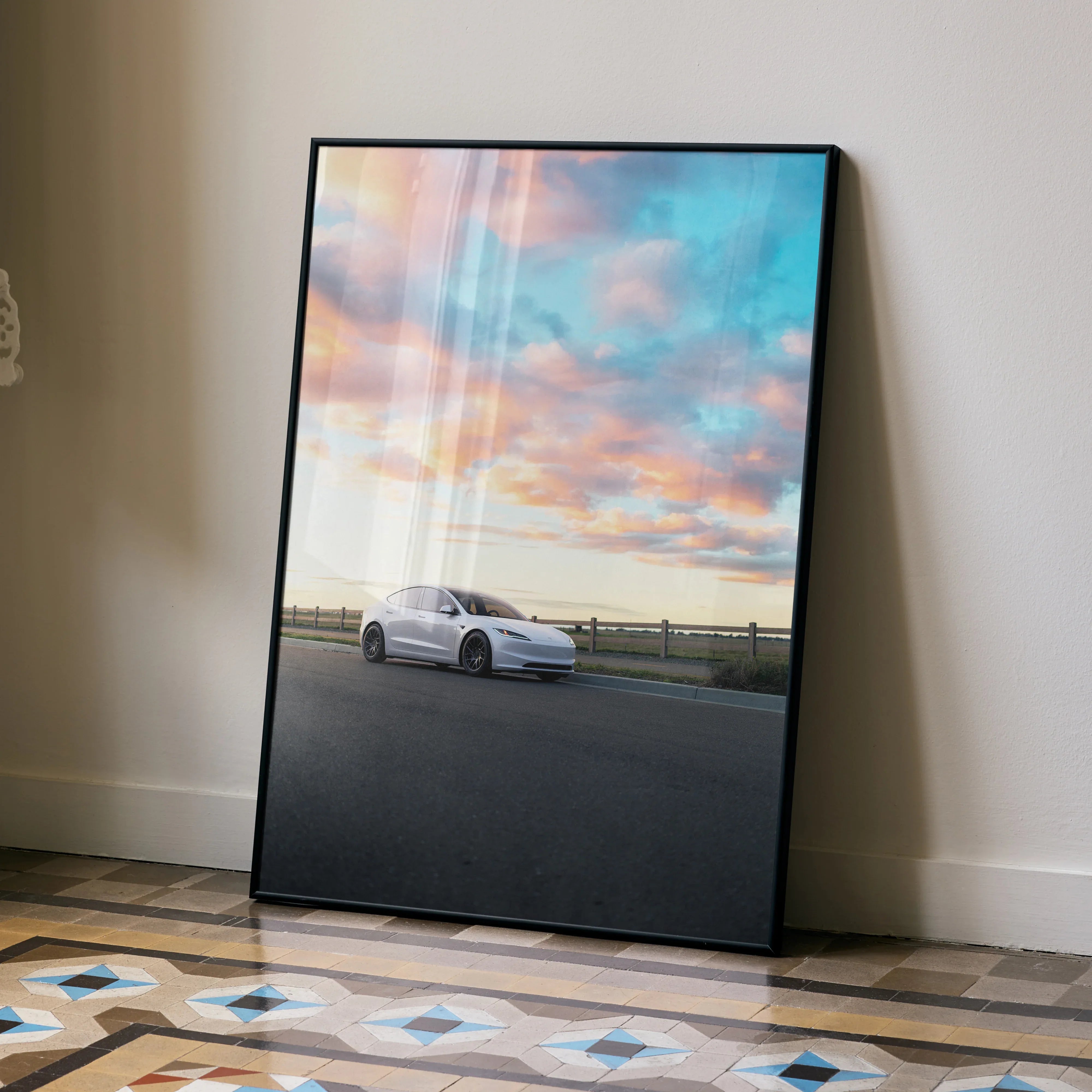 Tesla Model 3 Highland poster with sunset sky wall art in black frame leaning on wall.