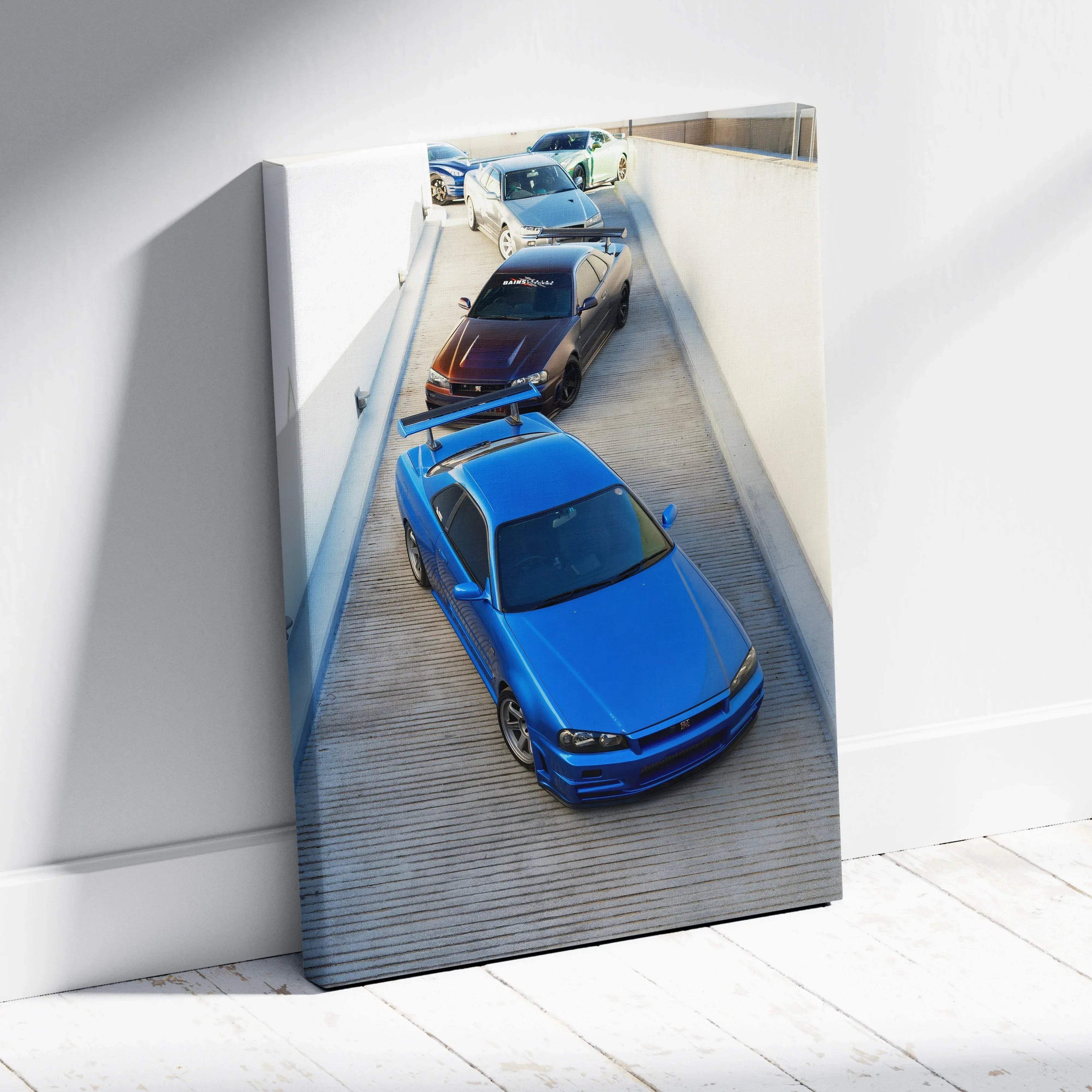 Vertical canvas wall art featuring three Nissan R34 GTRs in blue, gray, and black parked in a narrow alleyway.