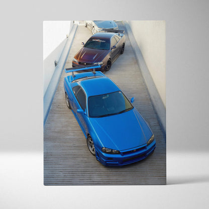 Vertical canvas wall art featuring high-resolution Nissan R34 GTR Skyline in blue and black cars on wooden driveway.