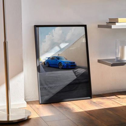 Nissan R34 GTR Skyline blue car poster displayed as framed wall art leaning against wall with sunlight.