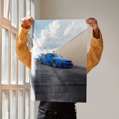 Poster of blue Nissan R34 GTR Skyline parked against angled concrete wall under cloudy sky, wall art.