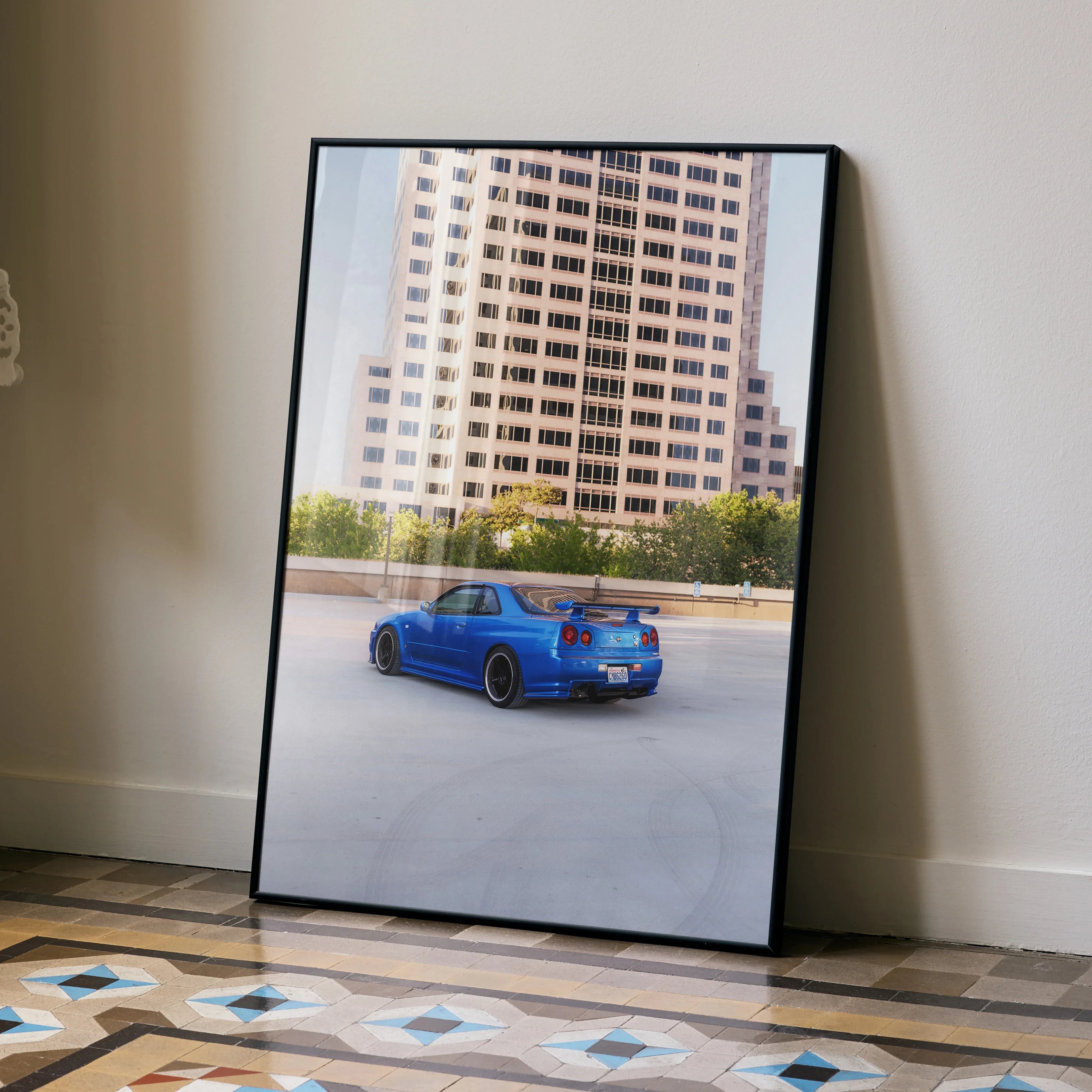 Nissan R34 GTR Skyline in vibrant blue on city street poster wall art with modern building background.