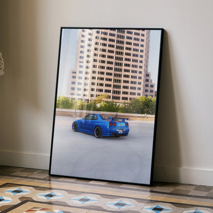 Nissan R34 GTR Skyline in vibrant blue on city street poster wall art with modern building background.