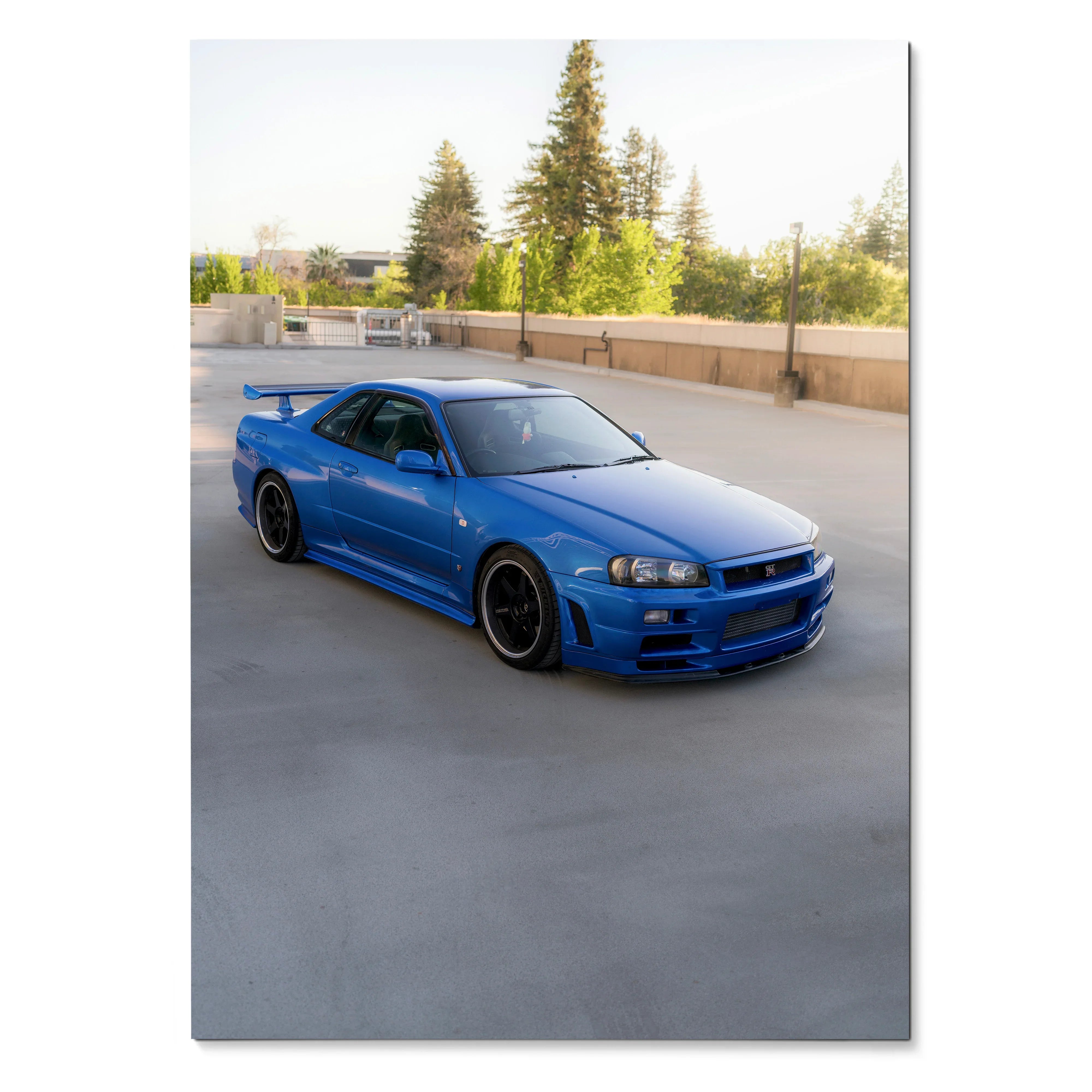 Nissan R34 GTR Skyline in blue on concrete surface with trees in background poster wall art.