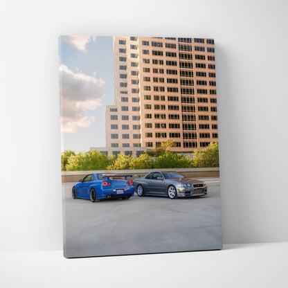 Vertical canvas wall art featuring blue Nissan R34 GTR and silver car in urban parking lot with building backdrop.