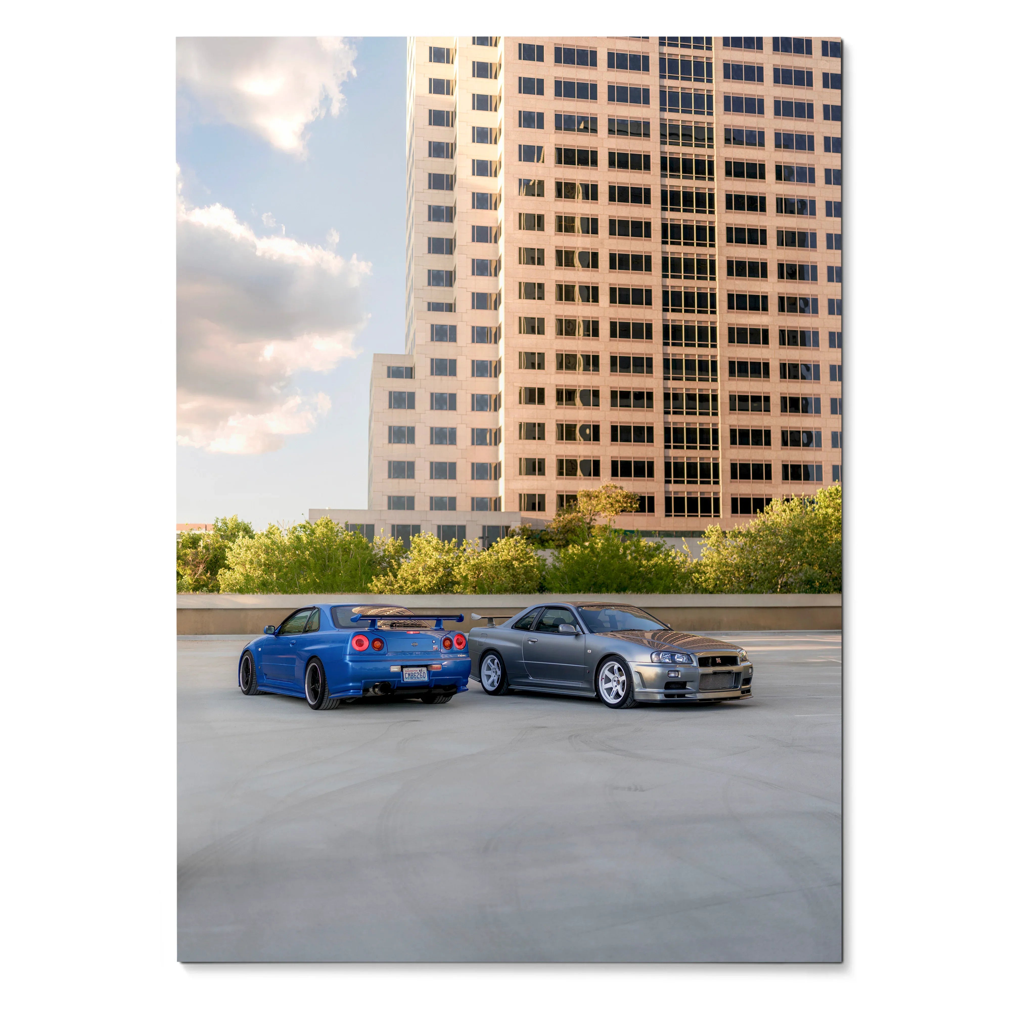 Poster of blue and silver Nissan R34 GTR Skyline cars parked on rooftop with cityscape background, wall art.