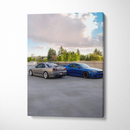 Vertical canvas wall art featuring two Nissan R34 GTR Skyline cars parked side by side under a partly cloudy sky.