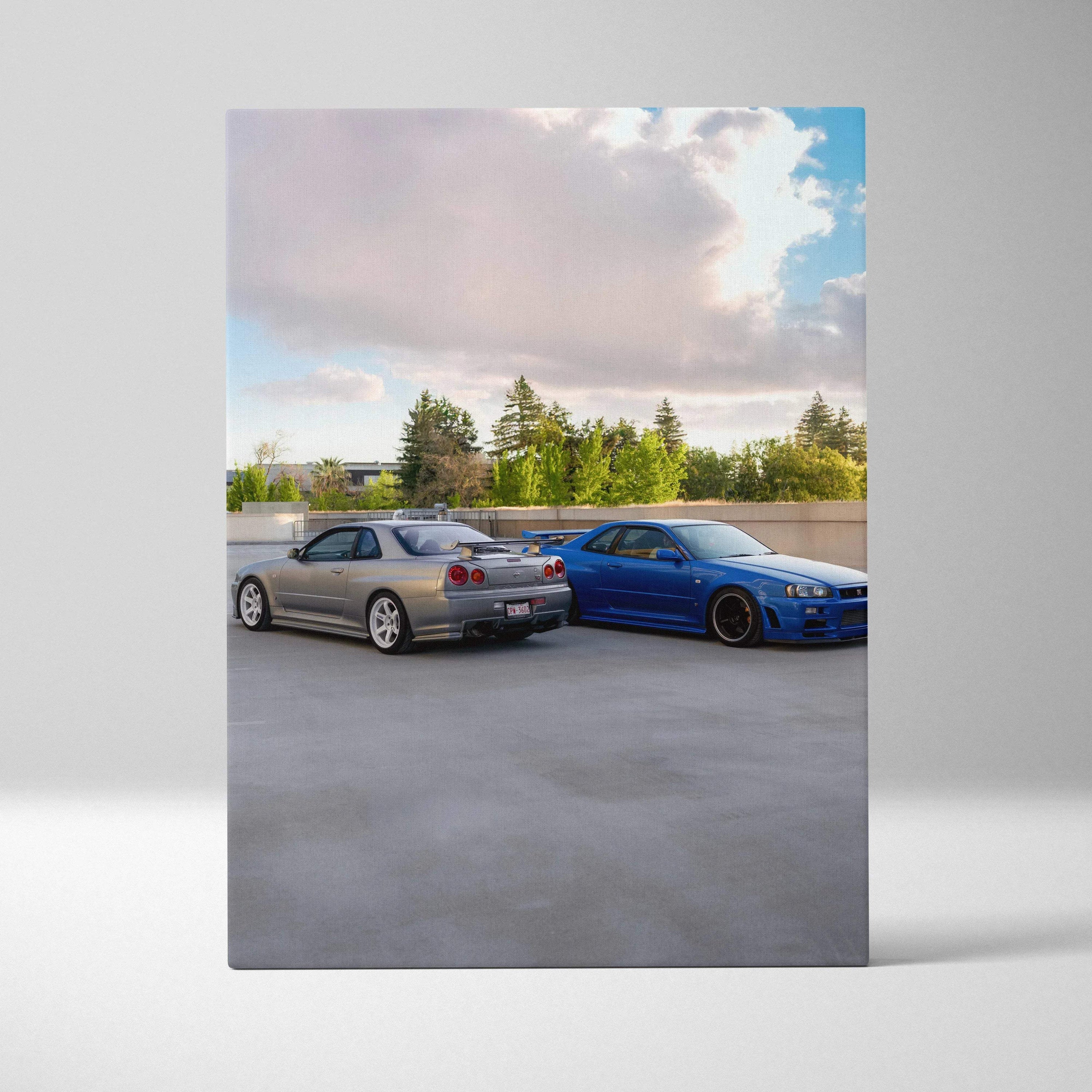 Canvas art featuring Nissan R34 GTR Skyline cars in silver and blue parked outdoors under a partly cloudy sky wall art.