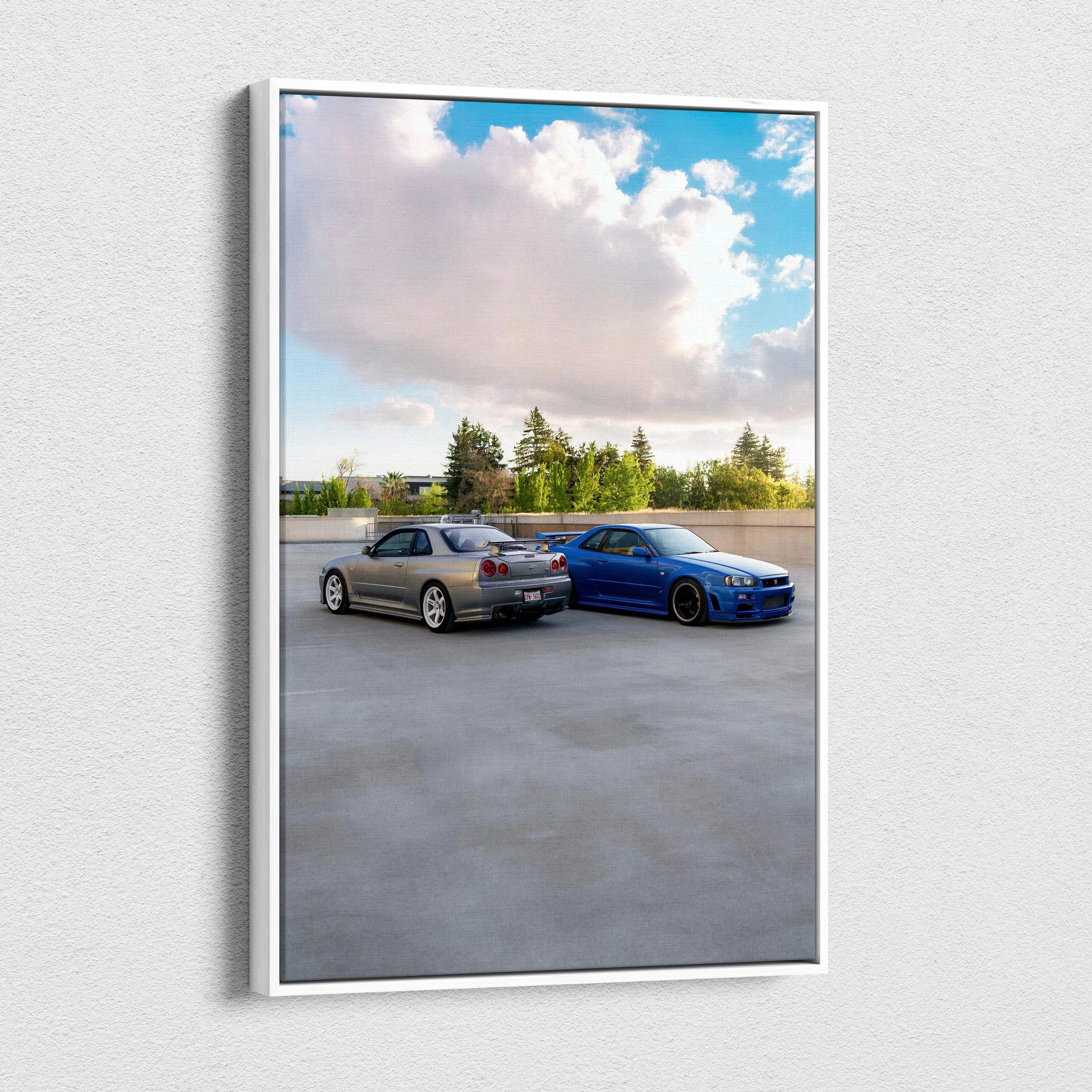 Canvas wall art featuring two Nissan GTR R34 Skyline cars parked on gray concrete under a blue sky with clouds.