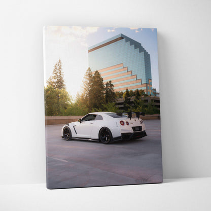 Vertical canvas wall art featuring a white Nissan R35 GTR parked in front of a reflective glass building at sunset.