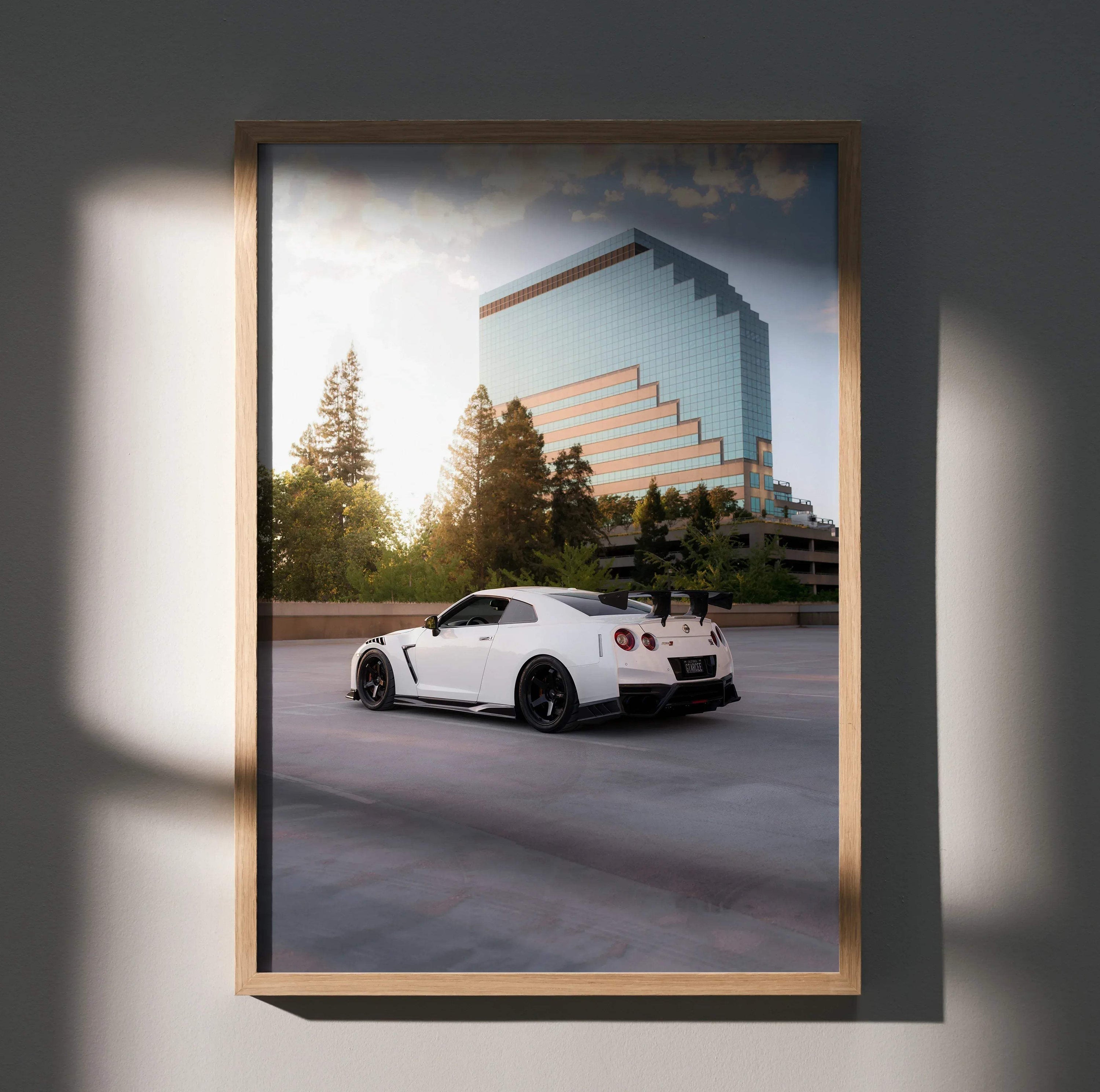 Nissan GTR R35 in white parked by modern glass building poster wall art with sunset lighting.