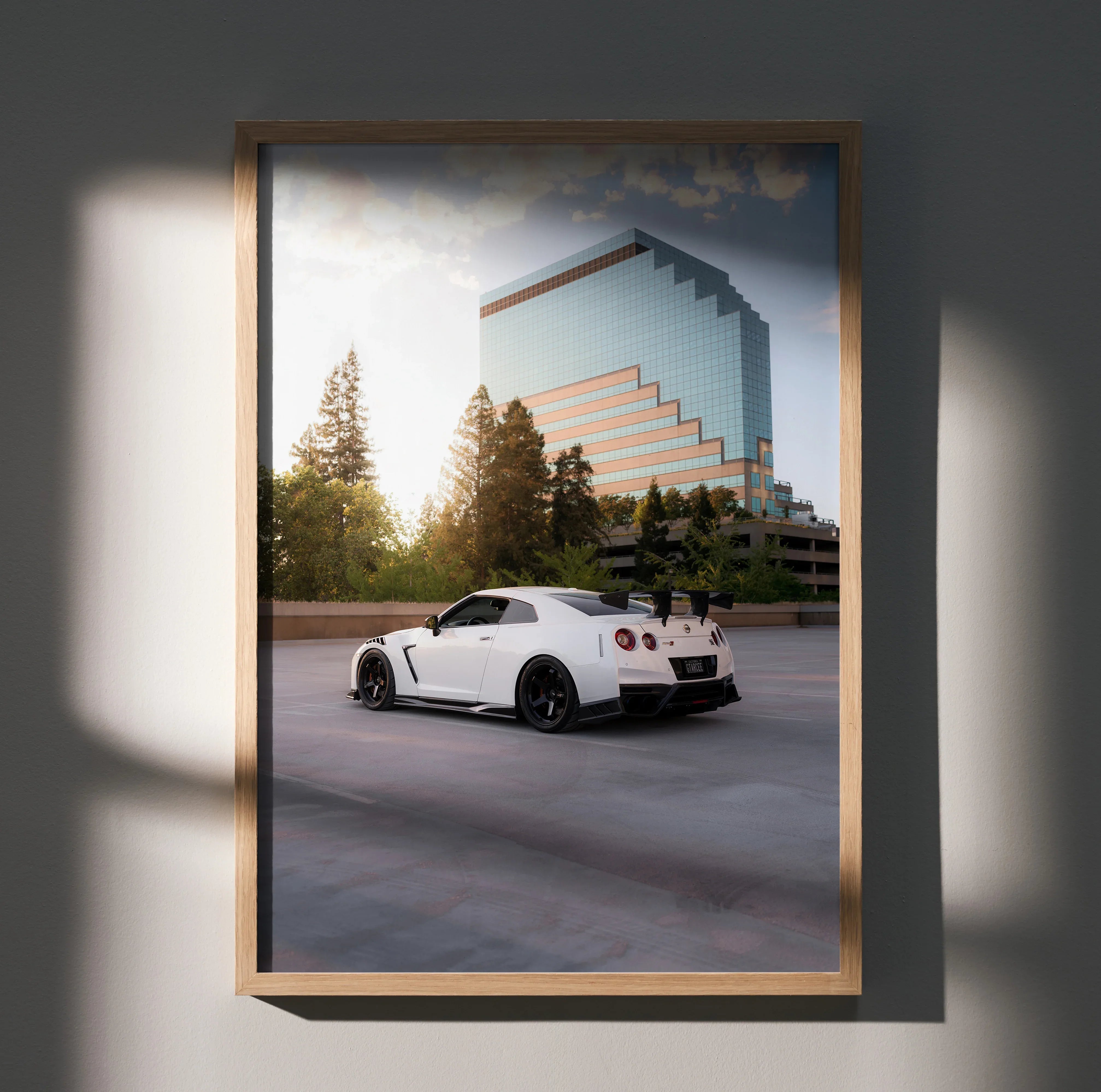 Nissan GTR R35 in white parked by modern glass building poster wall art with sunset lighting.