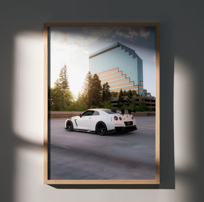Nissan GTR R35 in white parked by modern glass building poster wall art with sunset lighting.