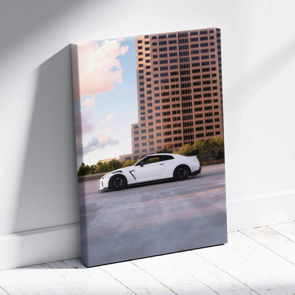 Vertical canvas wall art featuring a white Nissan R35 GTR parked against a sunset cityscape background.
