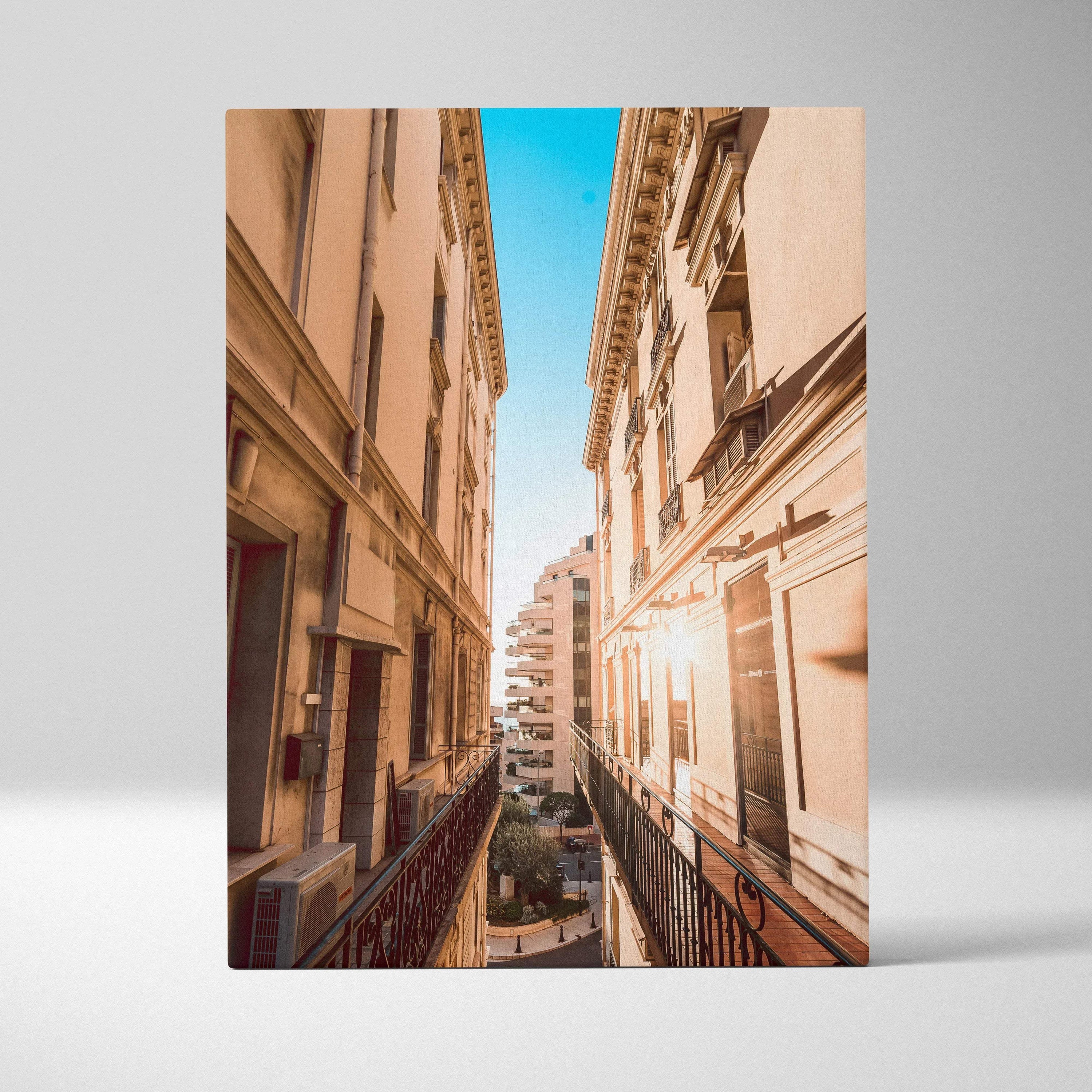 Tall beige buildings with intricate architectural details flank a narrow street under a bright blue sky on a canvas wall art.