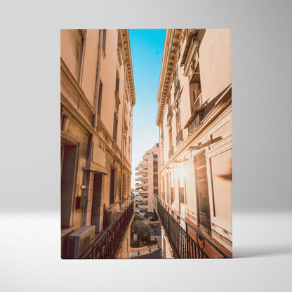 Tall beige buildings with intricate architectural details flank a narrow street under a bright blue sky on a canvas wall art.