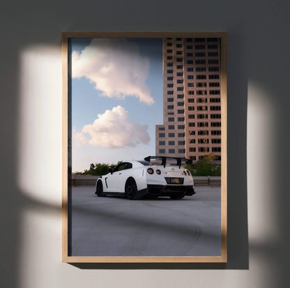 Nissan GTR R35 parked under blue sky with clouds and city buildings poster wall art.