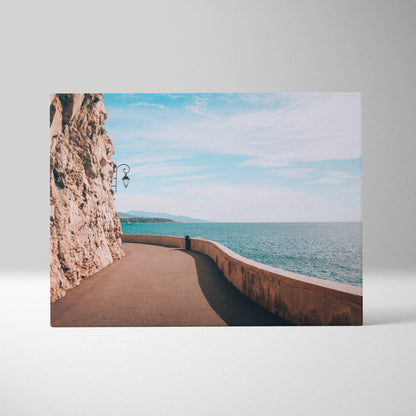 Canvas wall art of a coastal walkway beside rocky cliffs under a blue sky over ocean water.