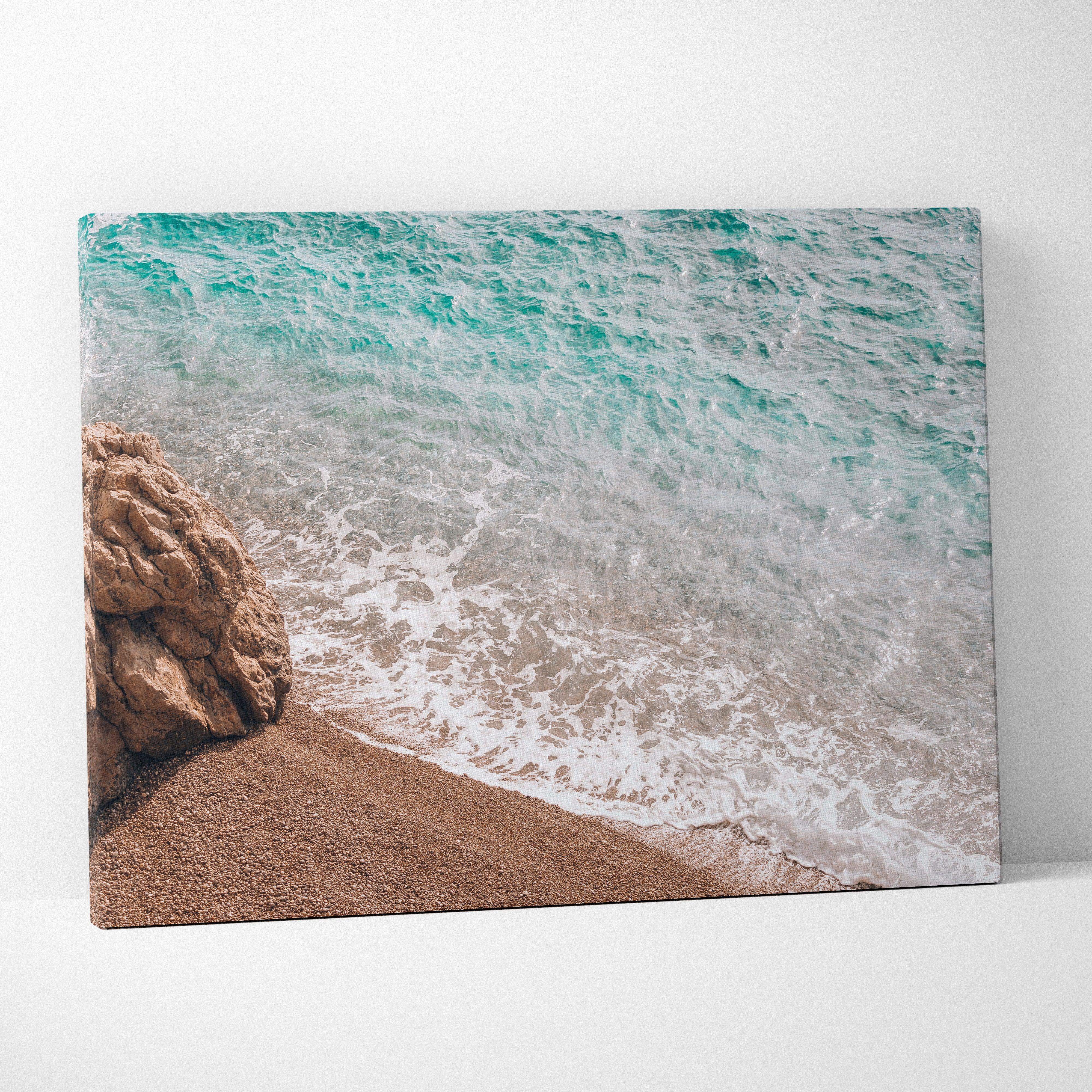 Vibrant turquoise ocean wave crashing on sandy beach with rugged rock canvas print