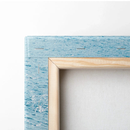 Close-up of stretched canvas art with light wood frame and blue textured beach design on canvas edge.