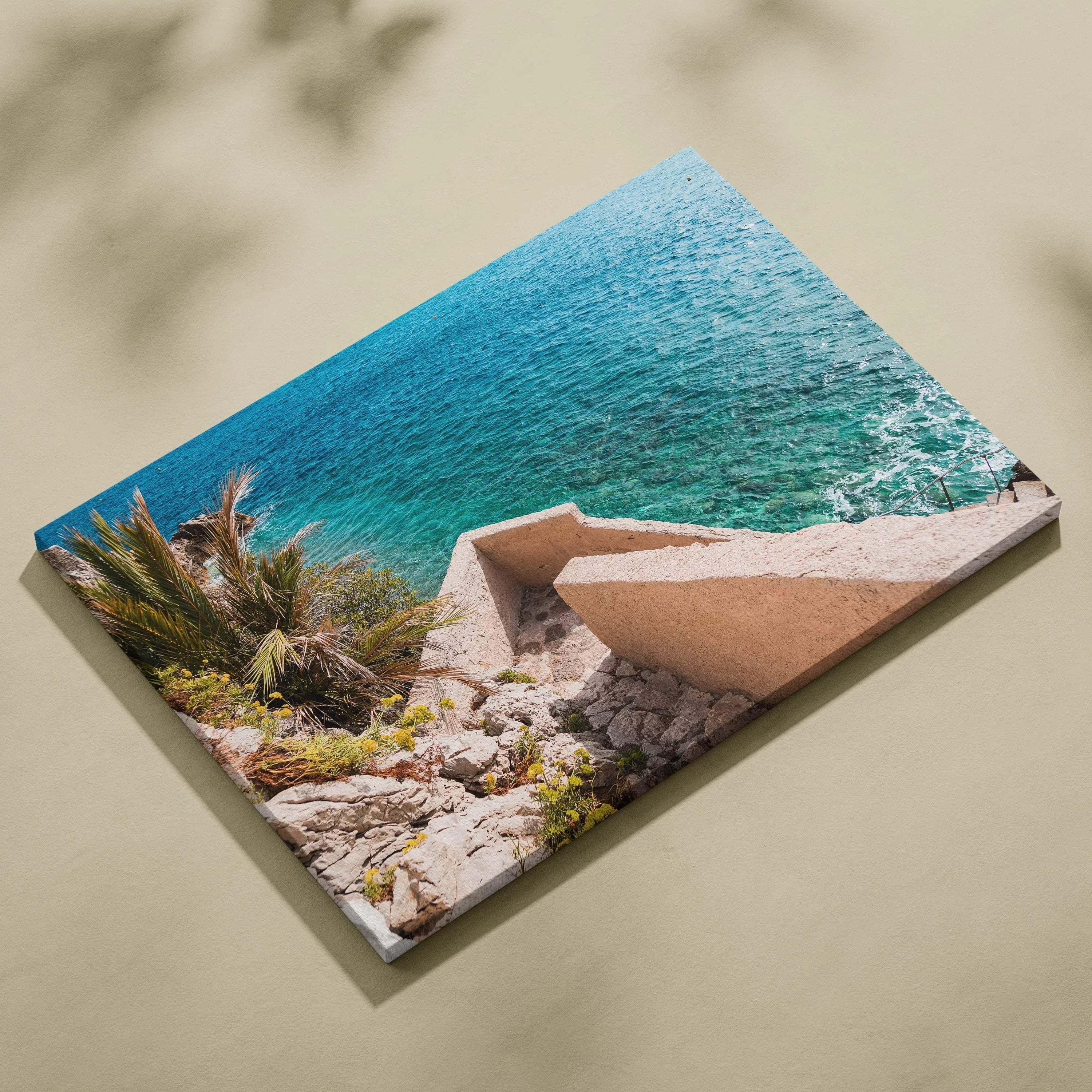 Canvas wall art featuring bright blue ocean waves meeting rocky shore with modern beige architectural structure.