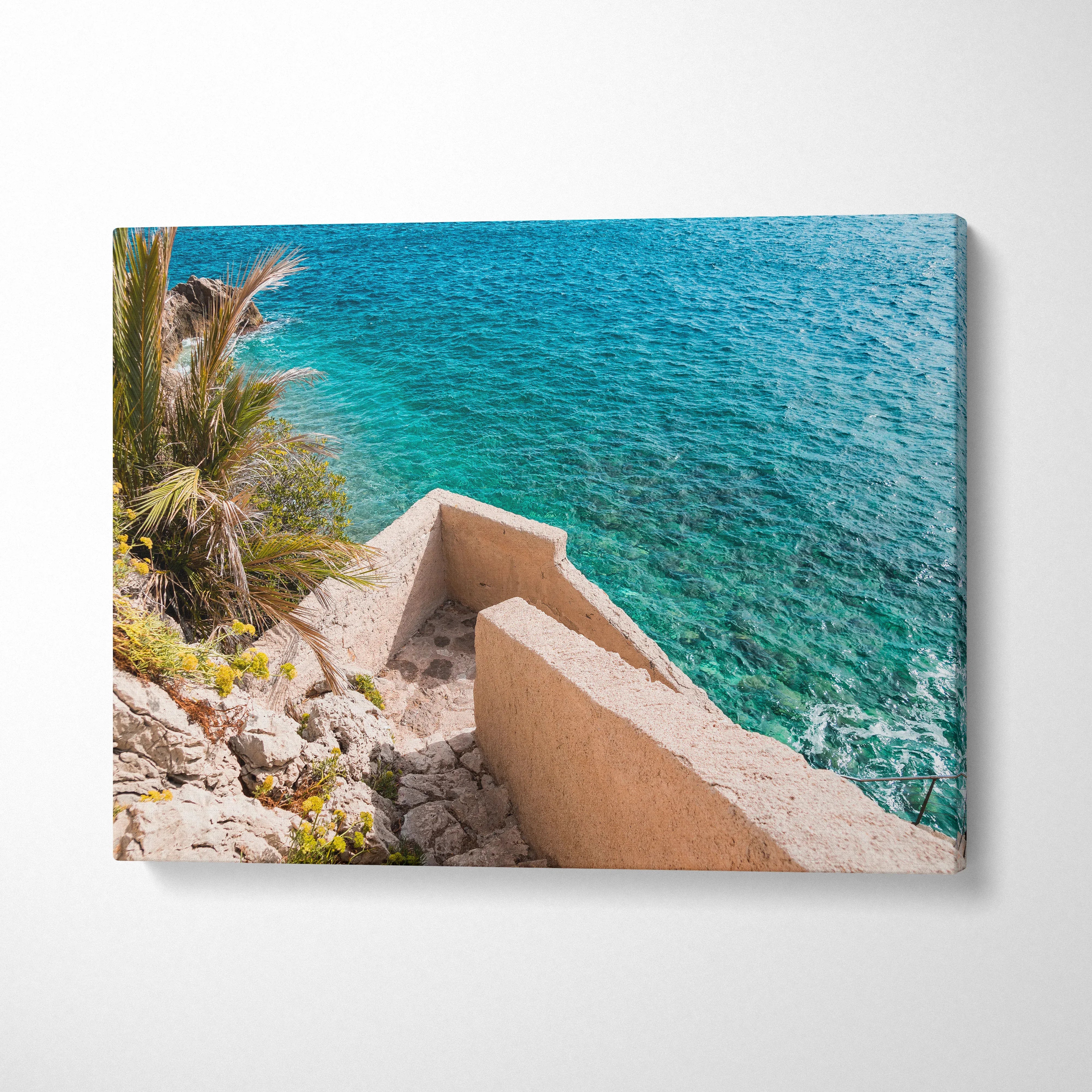 Canvas wall art featuring stunning architecture by a rocky beach with turquoise water.