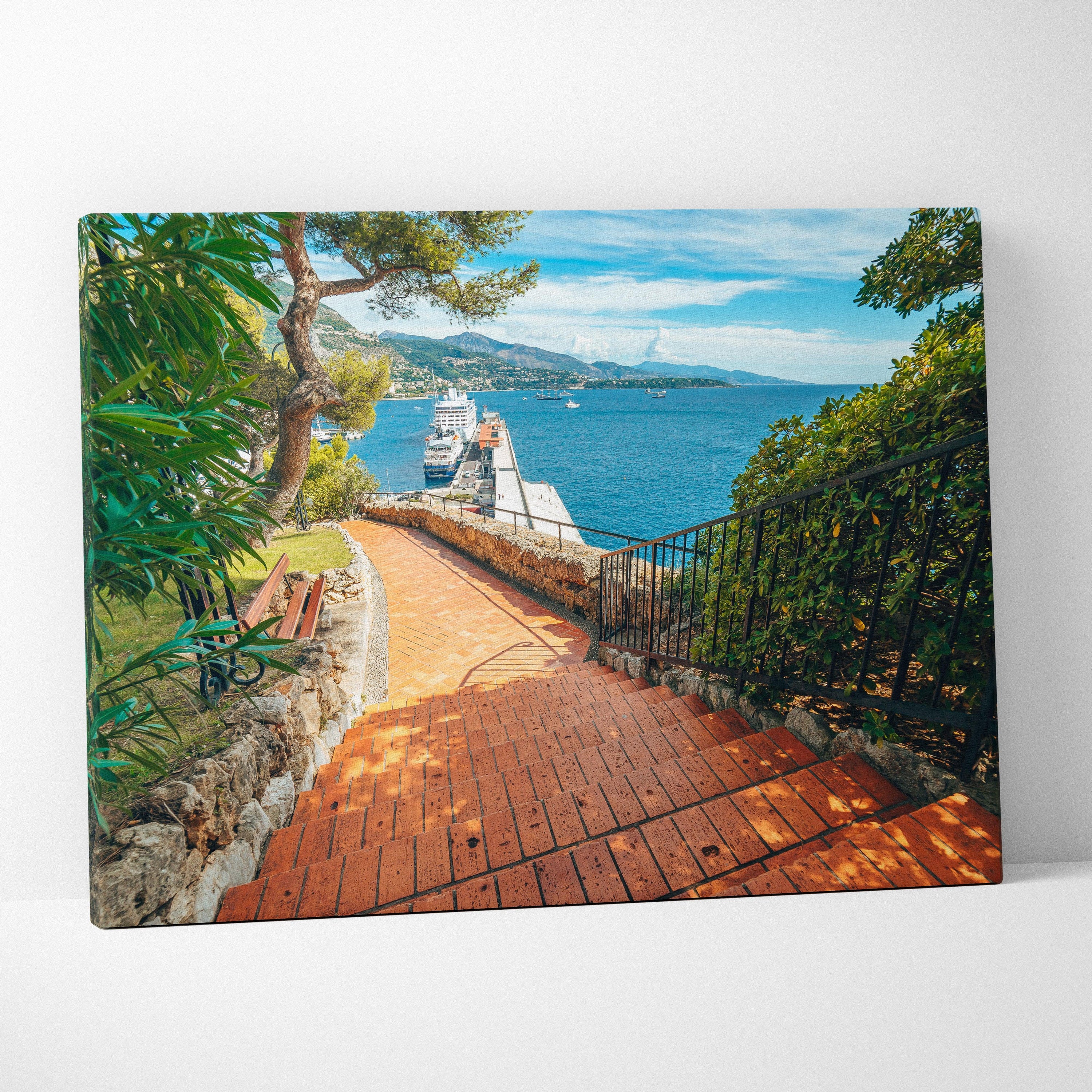 Canvas wall art featuring a sunlit brick pathway leading to a dock with boats, bordered by green trees and blue ocean.
