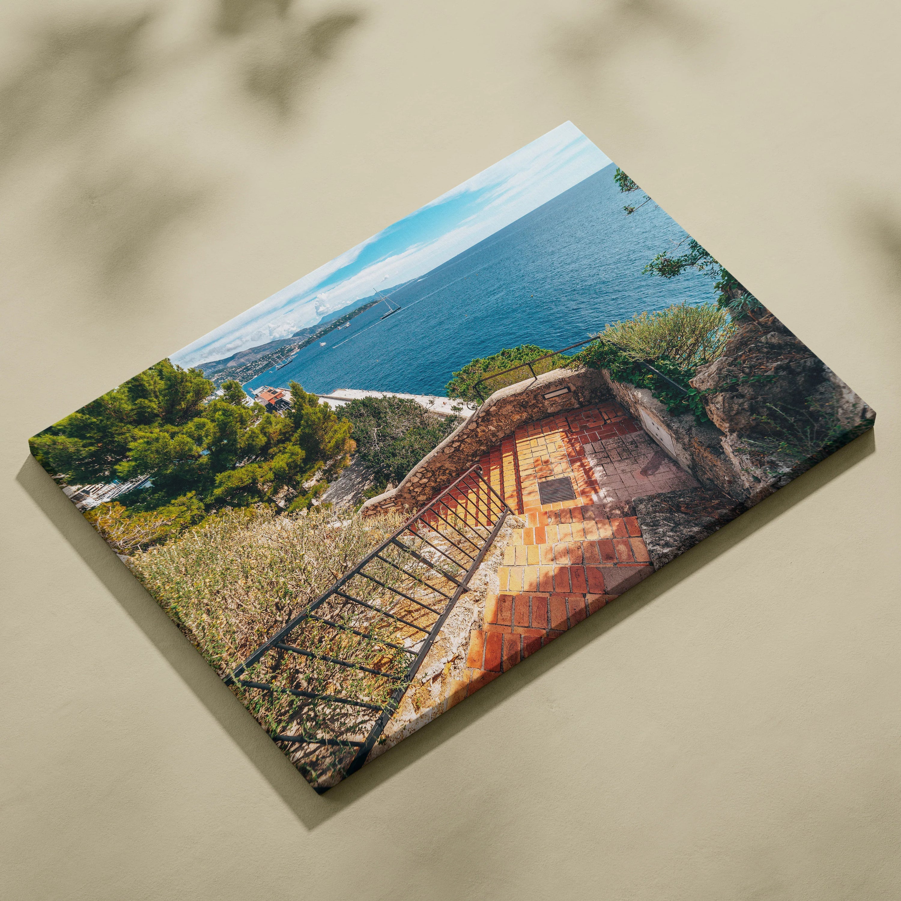 Canvas wall art featuring a sunlit stone terrace with wrought iron railing overlooking a blue ocean and coastal landscape.