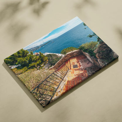 Canvas wall art featuring a sunlit stone terrace with wrought iron railing overlooking a blue ocean and coastal landscape.