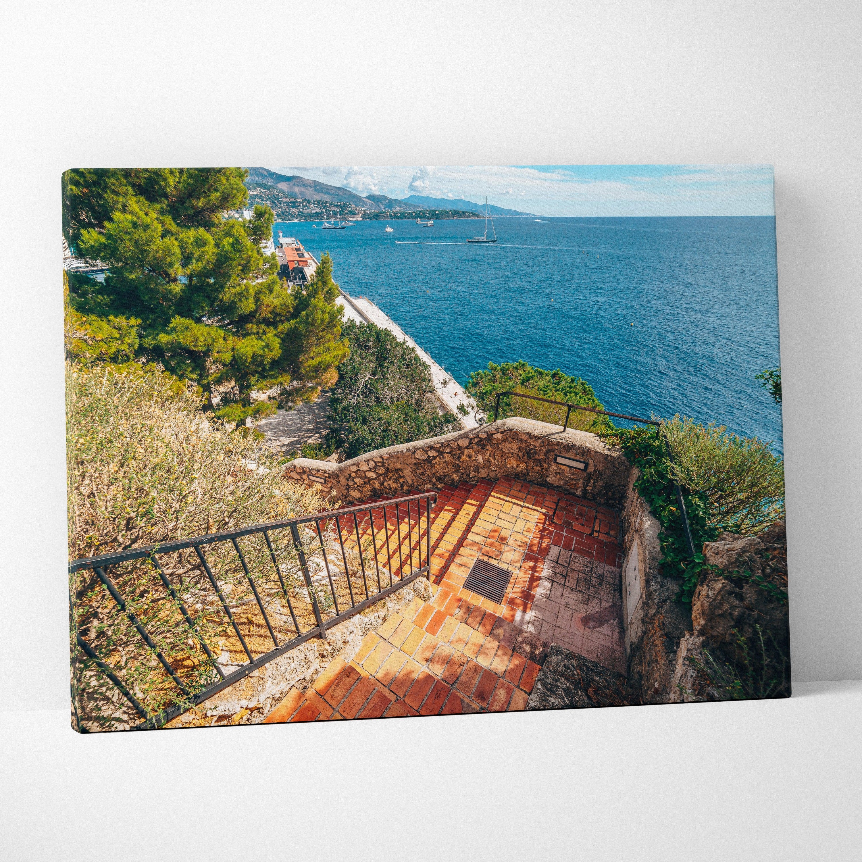 Canvas wall art of a coastal staircase with terracotta tiles and lush greenery overlooking a blue sea under a clear sky.