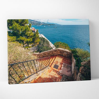 Canvas wall art of a coastal staircase with terracotta tiles and lush greenery overlooking a blue sea under a clear sky.