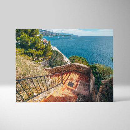 Canvas wall art featuring a sunlit coastal staircase with wrought iron railing overlooking blue ocean and greenery.