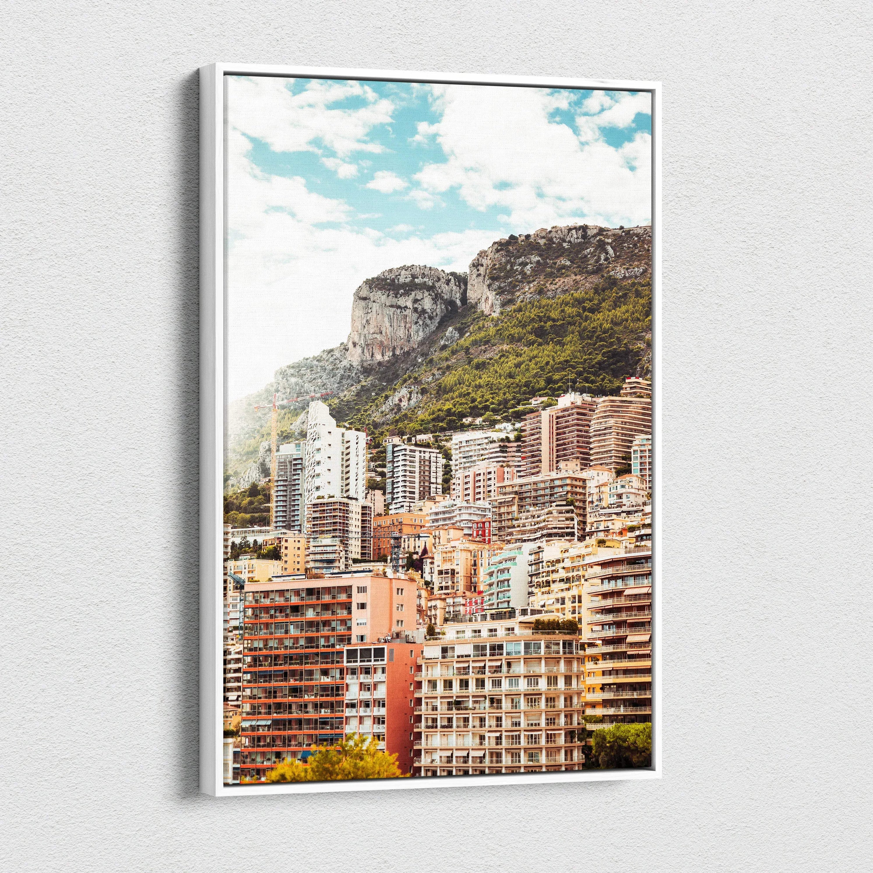 Framed canvas wall art featuring a vibrant cityscape with colorful buildings and rocky mountain backdrop under a blue sky.