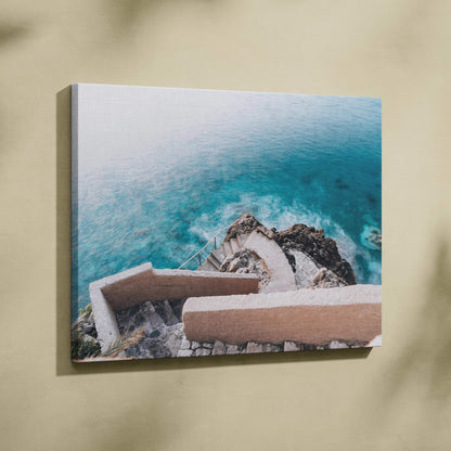 Coastal scene canvas art with blue ocean waves and beige architectural structures on cliffside.